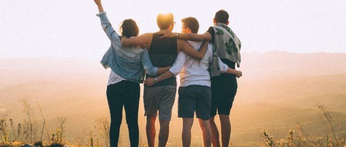 anonymous friends standing together at sunset in mountains