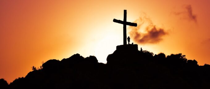 human standing beside crucifix statue on mountain