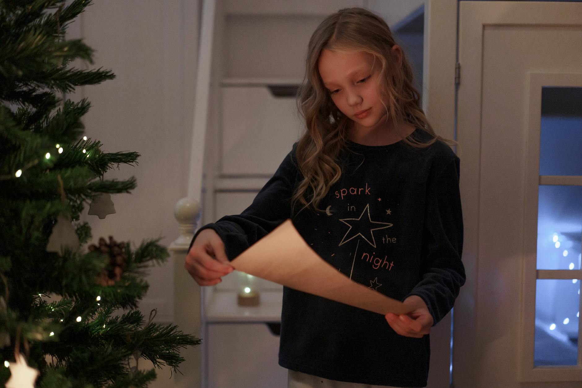 a young girl in black long sleeves reading a letter beside the christmas tree