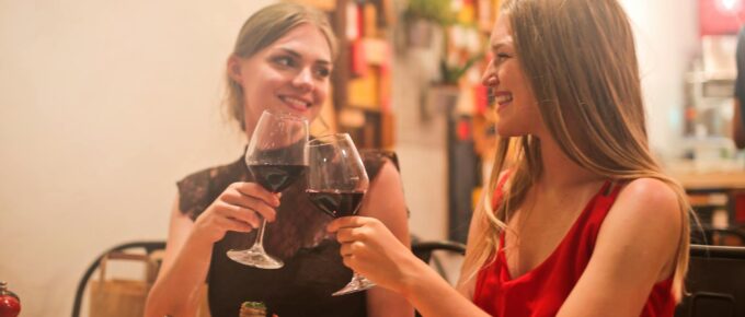 two women holding long stem wine glasses with red liquid