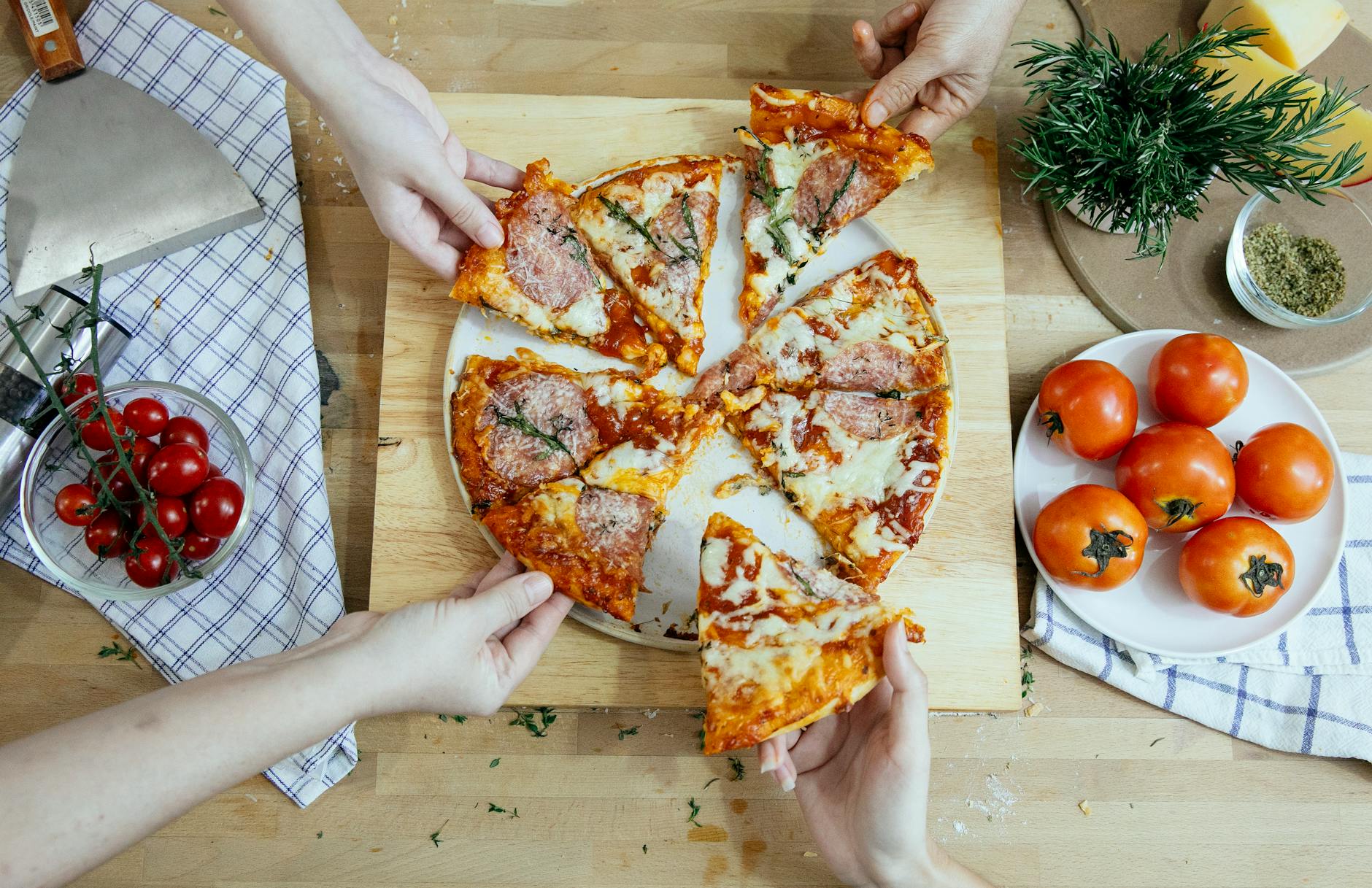 crop friends taking slices of delicious pizza from cutting board