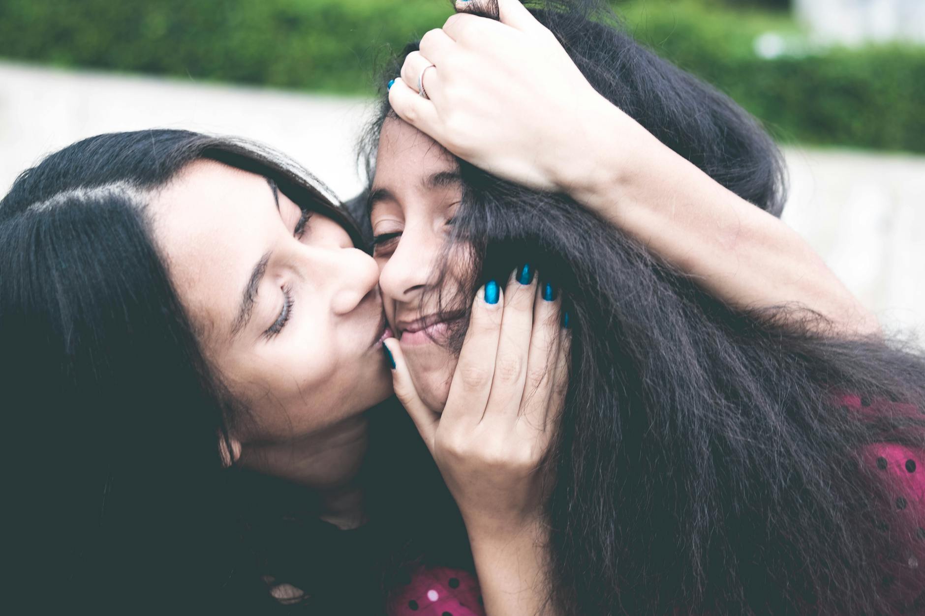 woman kissing cheek of girl wearing red and black polka dot top