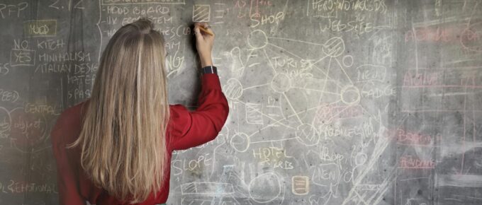 woman in red long sleeve writing on chalk board