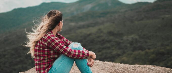 side view photo of woman sitting on ground overlooking a hill
